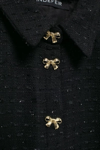 Détail du tissu en tweed noir aux paillettes argentées et boutons dorés en nœud papillon