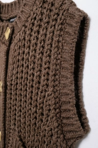 Detail of brown chunky knit vest with gold round buttons and ribbed textures