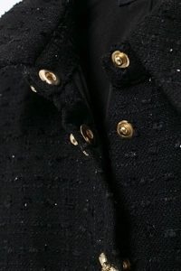 Détail macro du tissu en tweed noir avec bouton en métal doré sur la robe élégante