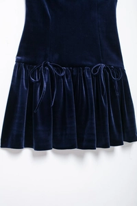 Détail d'une robe en velours bleu foncé avec ourlet à volants et nœuds délicats