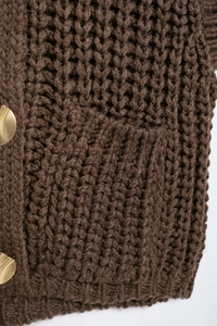 Detailed macro view of dark brown chunky knit texture and decorative gold button on vest