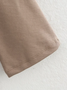 Close-up of double-needle stitching and cotton knit fabric on a brown asymmetric top