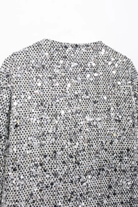 Dettaglio macro con paillettes d'argento scintillanti e tessuto a maglia bianco della giacca