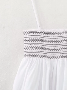 Detail of white cotton sundress featuring smocked chest and black geometric embroidery