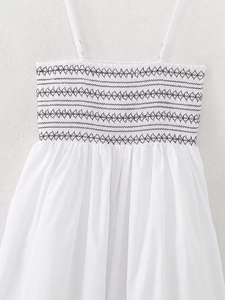 Close-up of white cotton dress featuring black geometric embroidery and pleated hemline