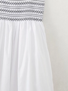 Detail view of smocking craft with black geometric diamond embroidery on white dress