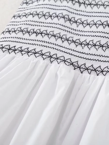Detail shot of white smocked poplin dress featuring black geometric embroidered stitching