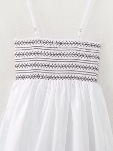 Close-up of black smocked geometric embroidery and thin straps on white poplin dress