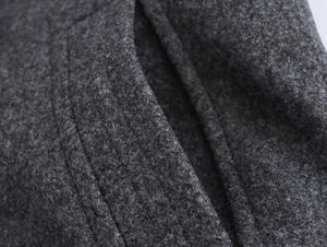 Macro shot of dark grey wool fabric texture and double-stitched pocket details on the coat