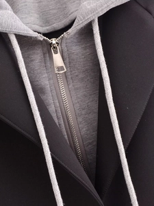 Detail of a black coat with a grey detachable knit hood and silver metal zipper puller