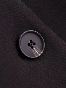 Detail shot of a black four-hole marble pattern button on wool blend coat fabric