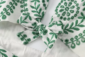 Dettaglio di abito in cotone bianco con ricamo di foglie verdi e nodo a fiocco