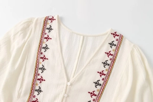 Detail of V-neckline with colorful ethnic embroidery on off-white cotton-linen dress