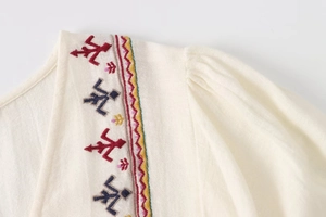 Detail of bohemian embroidery on beige cotton-linen dress with geometric patterns
