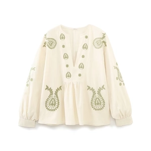 Détail du chemisier beige à col en V avec broderies florales paisley vertes fines