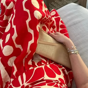 Detail of a beige woven envelope clutch paired with a red floral summer maxi dress