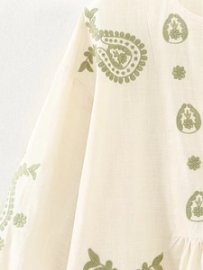 Détail de la broderie cachemire verte sur une blouse en coton et lin blanc cassé