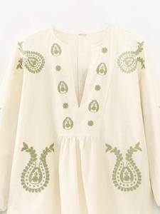 Détail du col en V avec broderie paisley verte sur une blouse beige en coton