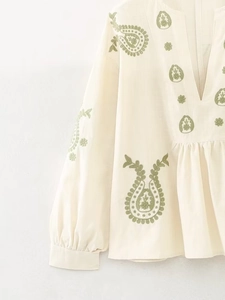 Détail de la blouse blanc cassé à col en V avec broderie paisley verte et texture lin
