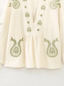 Détail du chemisier blanc cassé à col en V avec broderie paisley verte et plis élégants