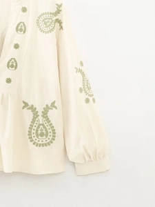 Détail de broderie paisley verte sur haut en coton crème à col en V et poignets plissés