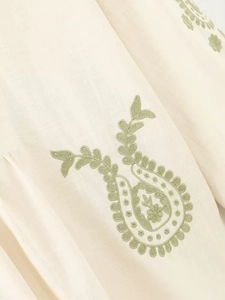 Gros plan du tissu en coton beige avec des broderies florales paisley vertes raffinées