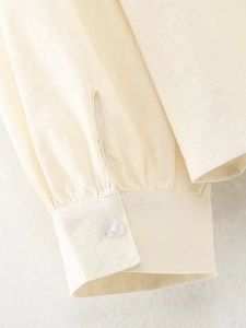 Détail de la manche en lin avec poignet plissé et bouton blanc sur chemisier beige