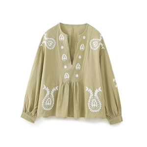 Détail de broderie florale blanche sur une blouse verte sauge à col en V et manches longues