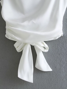 Detail of white satin top featuring an elegant large bow tie and side ruching texture