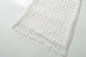Dettaglio dell'orlo dell'abito bianco a pois con cuciture sottili su tessuto leggero
