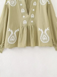 Détail de la blouse vert clair à col en V avec broderie blanche et texture coton