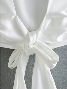 Detail shot of white satin top featuring a front tie knot design and silky fabric texture