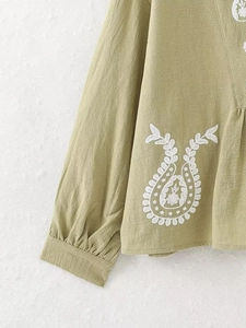 Gros plan d'une blouse en lin vert sauge avec broderie paisley blanche détaillée