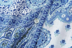Detailed macro view of paisley print blouse with a white shell button and fine stitching