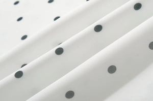 Dettaglio del tessuto bianco a pois neri con trama leggera e morbide pieghe naturali