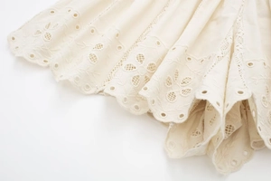 Detailed view of cream-white embroidery fabric with scalloped edges and floral patterns