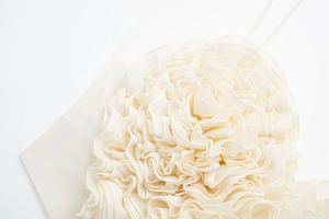 Vue détaillée des pétales de fleurs 3D en mousseline sur un caraco blanc d'été