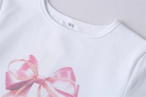 Gros plan d'un t-shirt blanc orné d'un imprimé nœud en ruban rose effet satiné