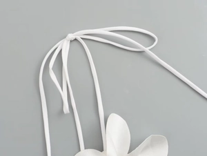 Macro shot of white halter strap detail with knotted cord and flower petal accent