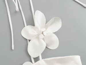 Detail view of a white halter top featuring a large 3D fabric flower and thin neck ties