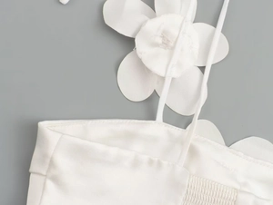Detailed close-up of white spaghetti strap top with large floral 3D flower decoration