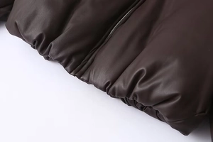Close-up of dark brown faux leather puffer jacket with silver metal zipper and hem