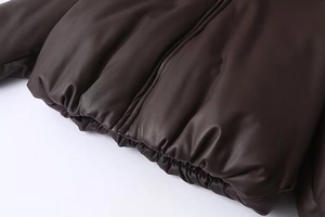 Close-up of dark brown faux leather puffer jacket with elastic hem and metal zipper