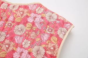 Gros plan détaillé du gilet matelassé rose à motif floral marguerite et bordure beige
