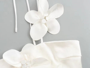 Close-up of white satin camisole featuring 3D floral appliqué and elegant button detail