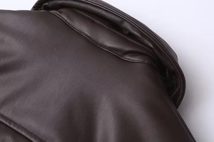 Close-up of deep brown vegan leather texture and fine stitching on a padded winter jacket