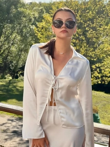 Detailed close-up of a pearly white satin shirt featuring front bow ties and flared sleeves