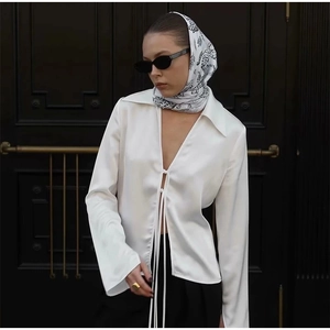 Detail of white satin long sleeve blouse with elegant bow tie closure and V-neck design