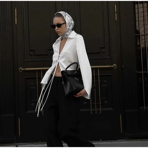 Detail of a white satin V-neck blouse with a metal buckle and high-waisted trousers