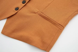 Detail view of orange linen vest fabric with deep brown buttons and fine pocket stitching